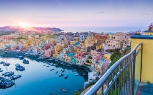 Sunset view of serene sea, fishing and sightseeing boats, cafes and restaurants in Marina Corricella, Procida Island, Italy.