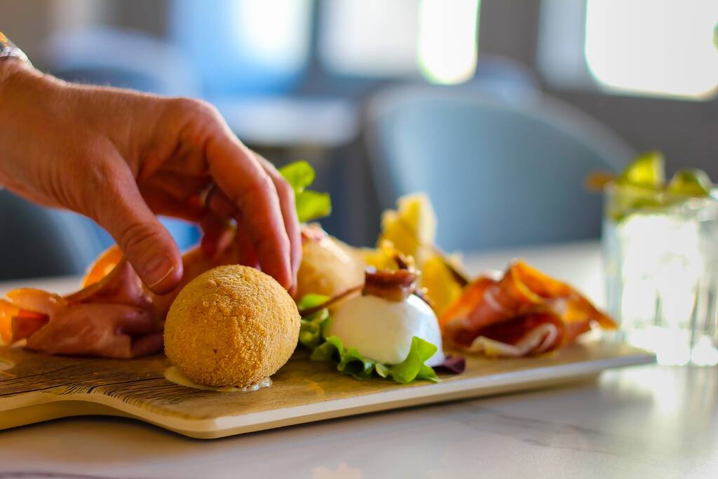 hand taking a croquette from a tray of typical Napolitan snacks such as buffalo mozzarella, savory puff pastry, black pig salami from Caserta, ham and cheese