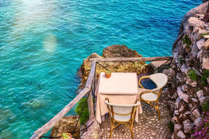 A pretty table for two in a secluded seaside setting beside the shallow blue water of the Amalfi Coast in Italy.