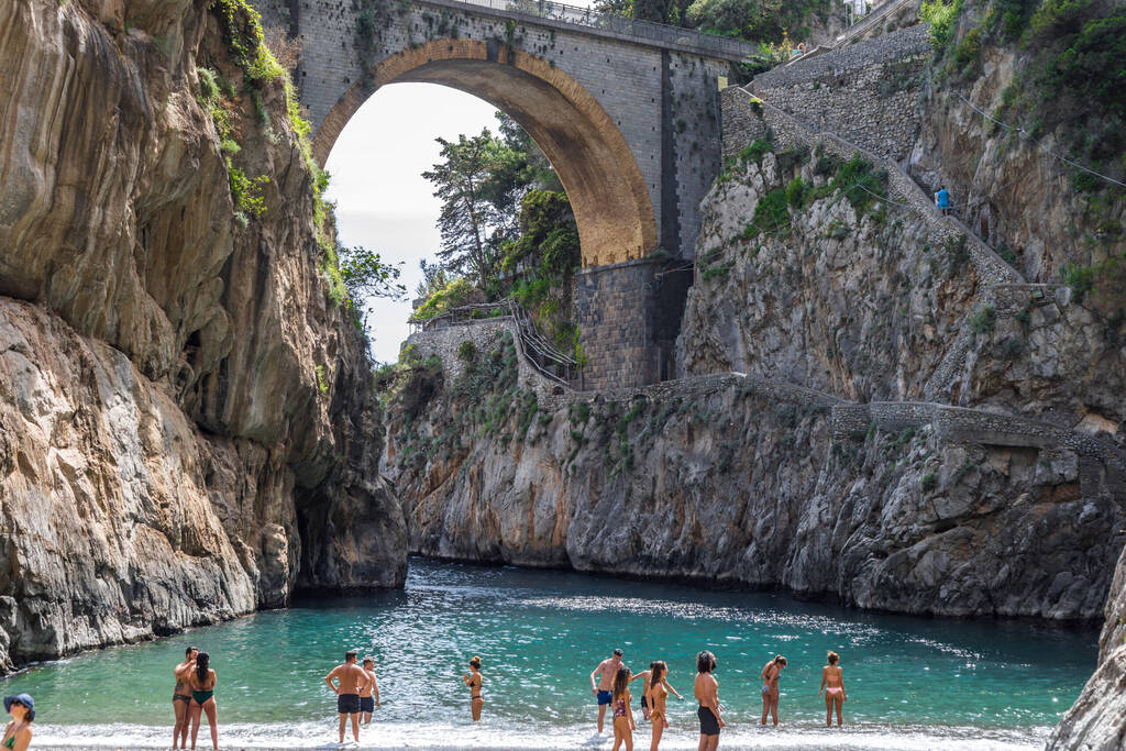 Fiordo di Furore beach. Furore Fjord, Amalfi Coast, Positano, Naples, Italy. May 2018 - Tourists standing at the beach and into the turquoise Mediterranean beach. The bridge over the fjord.