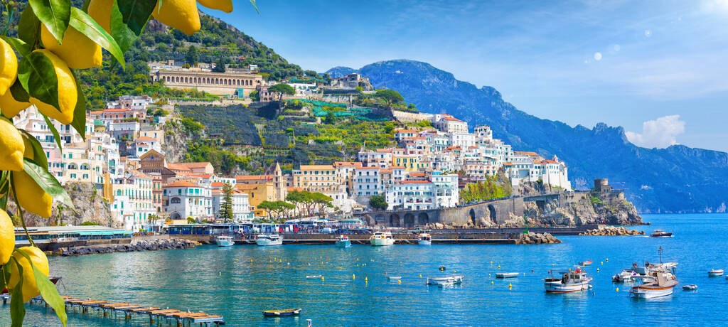Panoramiczny widok na piękne Amalfi na wzgórzach prowadzących w dół do wybrzeża, Kampania, Włochy. Wybrzeże Amalfi jest najpopularniejszym miejscem podróży i wypoczynku w Europie. Dojrzałe żółte cytryny na pierwszym planie.