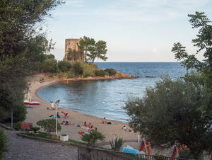 Santa Maria Navarrese, Sardinia, Italy, September 6, 2020: view of Spiaggia di Santa Maria Navarrese beach with group of relaxing people, green trees and old stone tower. Golden hour light.