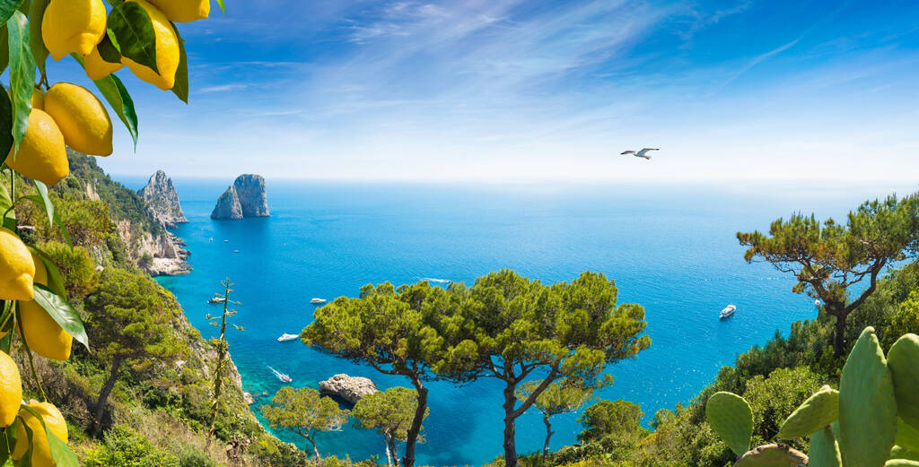 Welcome to Capri concept. Panoramic image with Faraglioni Rocks near Capri Island, Italy. Beautiful paradise landscape with azure sea in summer sunny day and ripe yellow lemons.