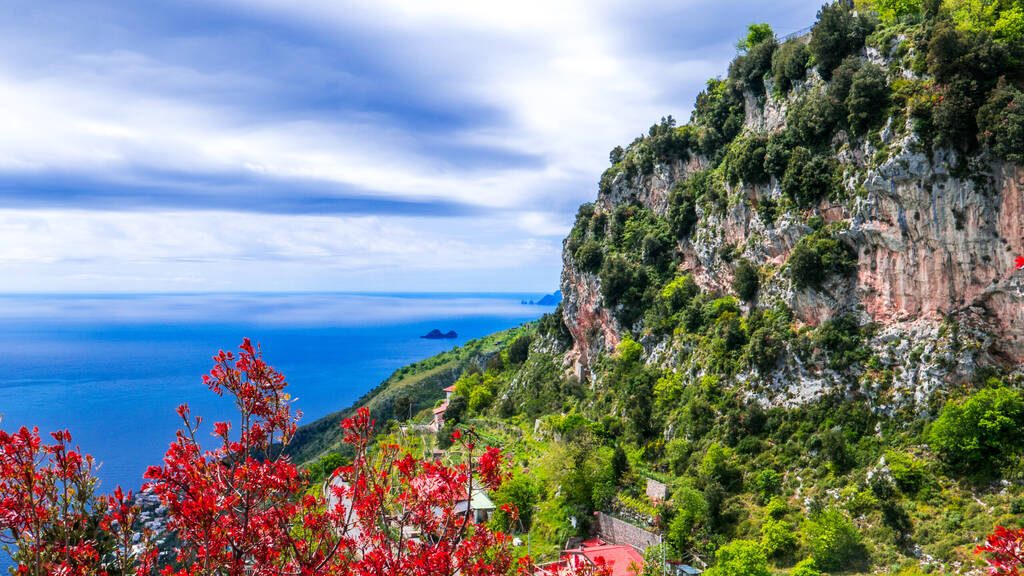 Panoramic view of the Amalfi coastline, with vertical rocky cliffs and luxuriant vegetation, against a deep blue Mediterranean sea. Amalfi Costline, Naples, Italy.