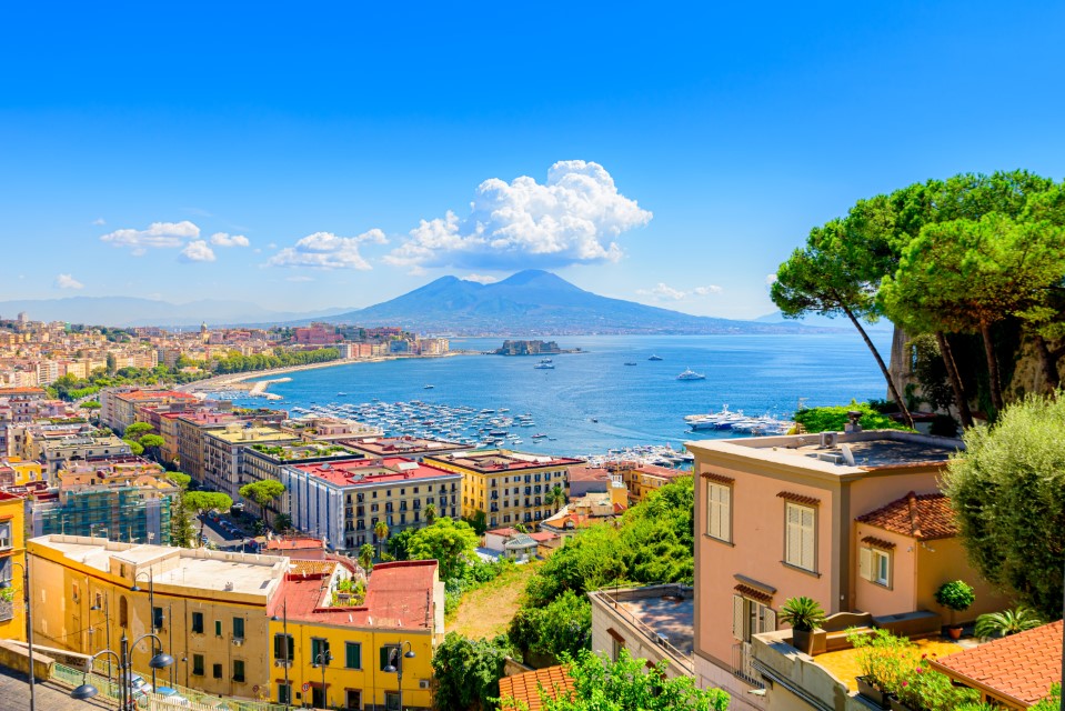 Czy warto odwiedzić Neapol?, Naples, Italy. View of the Gulf of Naples from the Posillipo hill with Mount Vesuvius far in the background and some pine trees in foreground. August 31, 2021.